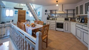 Une cuisine avec des meubles blancs, une table à manger avec des chaises, un escalier et une vue sur l’extérieur.
