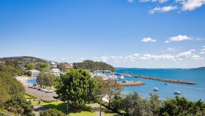 Marina costeira com barcos atracados, área de estacionamento e edifícios ao fundo.