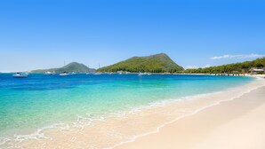 Uma praia com águas turquesa cristalinas, barcos e uma montanha ao fundo.