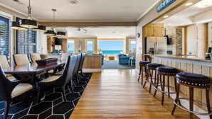 A spacious kitchen with a view of the ocean, a dining area with a large table and chairs, and a bar with stools.