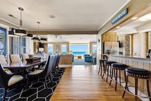 A spacious kitchen with a view of the ocean, a dining area with a large table and chairs, and a bar with stools.