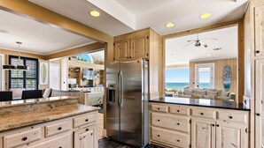 A kitchen with wooden cabinets, a stainless steel refrigerator, and a view of the ocean.