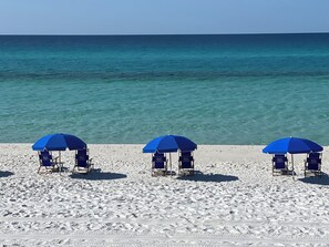 Ein Strand mit drei blauen Sonnenschirmen und Liegestühlen.