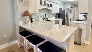 A kitchen with a large island, white cabinets, and a trash can. - Amazing Sunsets, Sugar White Sand, Gulf Front (Fort Walton Beach)