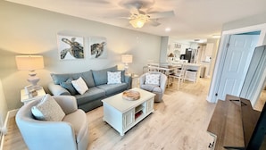 A living room with a sofa, armchair, coffee table, and a dining area with chairs and a table. - Amazing Sunsets, Sugar White Sand, Gulf Front (Fort Walton Beach)