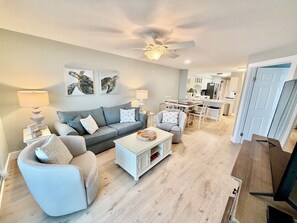 A living room with a sofa, armchair, coffee table, and a dining area with chairs and a table.