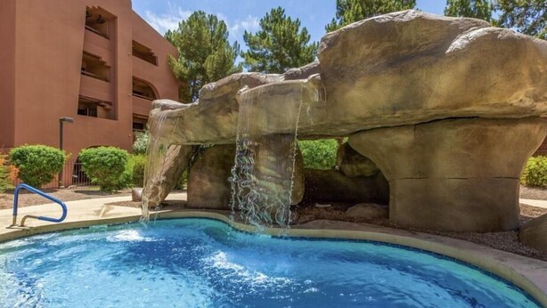 Una piscina con una cascata, circondata da grandi formazioni rocciose e un edificio con balconi.