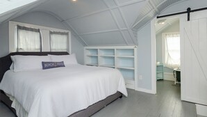 Une chambre à coucher avec un lit, un oreiller orné du texte « Beach House », des étagères intégrées et un puits de lumière.