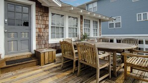 Une terrasse en bois avec une table et des chaises, une porte grise et une maison bleue en arrière-plan.