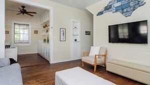 Un salon équipé d’un téléviseur, d’un ventilateur de plafond, d’un banc en bois, d’un canapé et d’une fenêtre avec des stores.