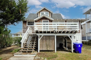 A two-story house with a wooden deck and a staircase leading to a second-floor balcony.