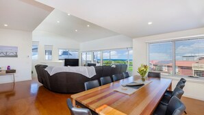 A spacious living area with a large sofa, a wooden dining table, and a view of the ocean. - Southern Waves - Views of the Southern Ocean (Port Fairy)