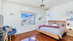 A bedroom with a wooden bed, a desk with a chair, a window with a view, and a ceiling light. - Southern Waves - Views of the Southern Ocean (Port Fairy)