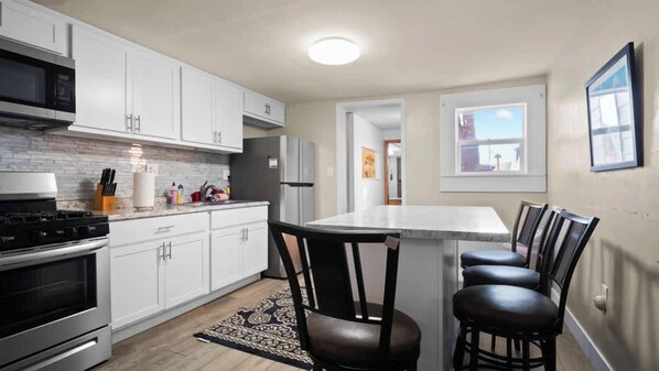 A modern kitchen with white cabinets, a central island with bar stools, a microwave, and a refrigerator.