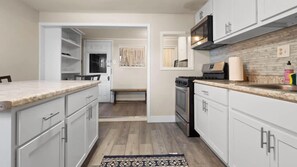 A kitchen with white cabinets, a microwave, stove, and a small dining area with a bench.