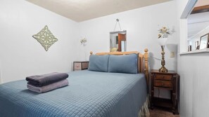 A bedroom with a bed, a nightstand, a mirror, and a wall decoration.