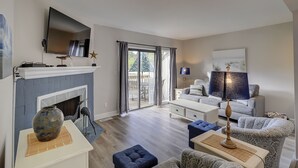 Een moderne woonkamer met een open haard, een flatscreen televisie, een eethoek met een tafel en stoelen, en een groot raam met gordijnen.