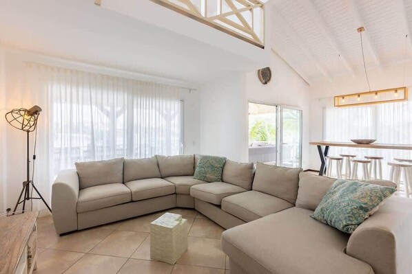 A modern living room with a beige sectional sofa, a floor lamp, and a dining area with a table and chairs.