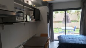 Ein kompaktes Hotelzimmer mit Küchenzeile, einem Bett, einem Esstisch und Blick ins Freie.