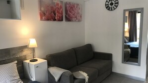 Ein modernes Schlafzimmer mit einer grauen Couch, einem Nachttisch mit Lampe sowie zwei floralen Bildern an der Wand.