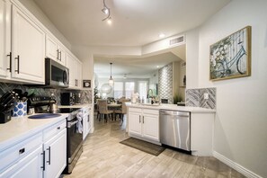 A modern kitchen with white cabinetry, a built-in microwave, and a dishwasher. There is a dining area with a table and chairs, and a kitchen island with a sink. - Kierland Scottsdale 2BR | Gated, Pool, Spa, 2 car Garage (Phoenix)