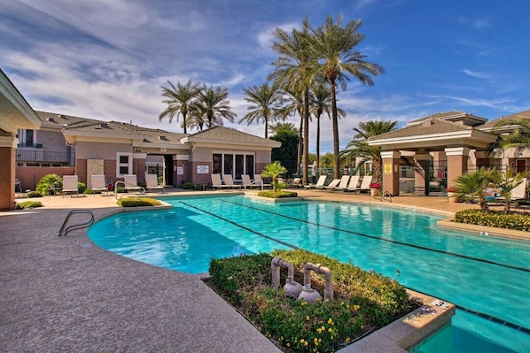 A swimming pool with lounge chairs, palm trees, and a clear sky.