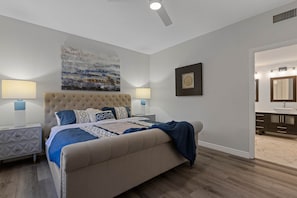 A bedroom with a tufted headboard, a large abstract painting, two bedside lamps, a bed with a blue and white bedspread, and a wooden floor. - Kierland Scottsdale 2BR | Gated, Pool, Spa, 2 car Garage (Phoenix)