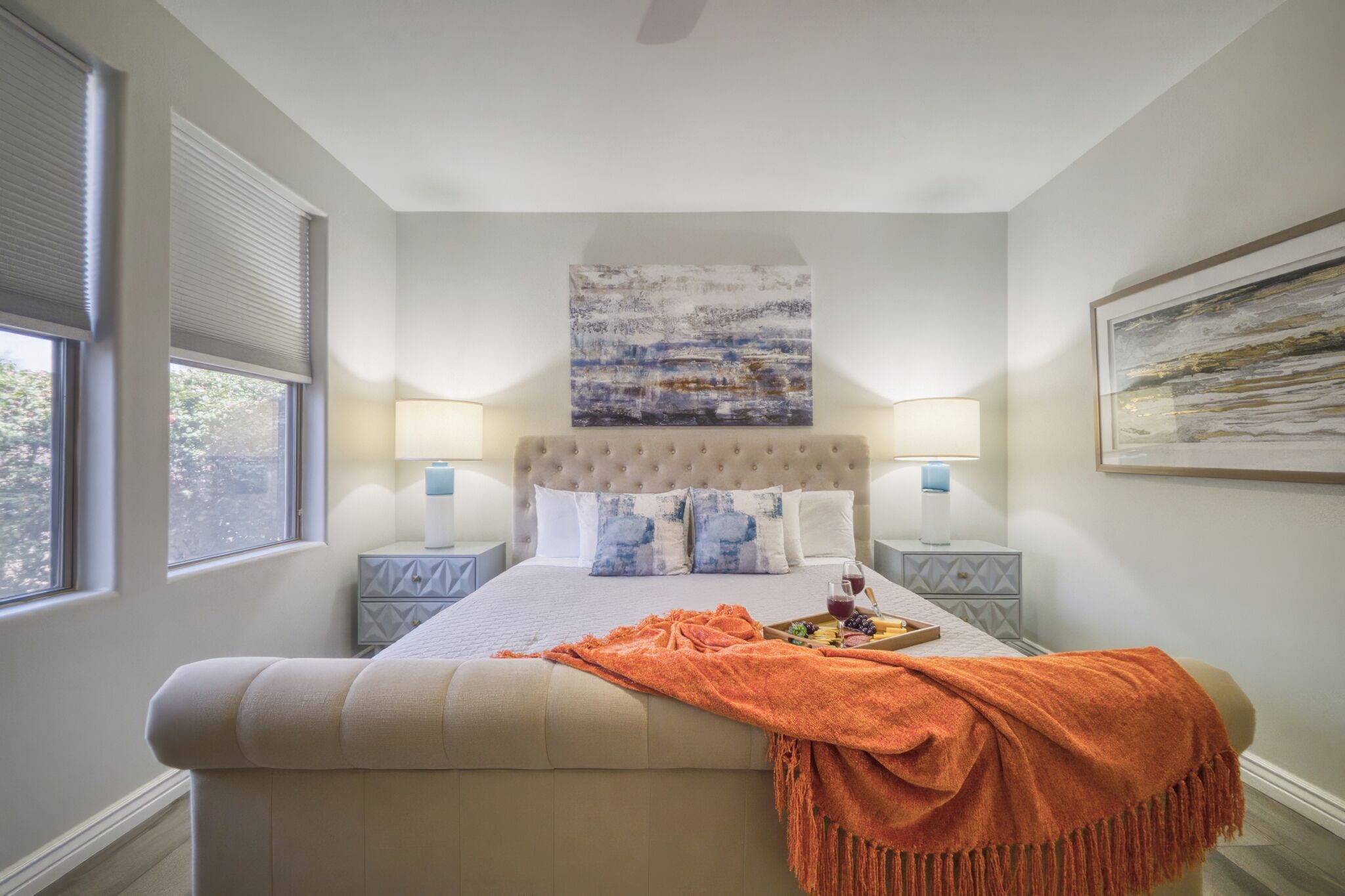 A bedroom with a large bed, two bedside tables, a headboard, and artwork on the walls.