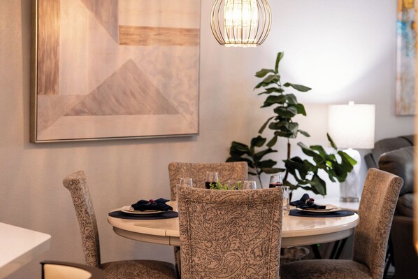 A dining area with a round table, patterned chairs, a hanging light fixture, and a framed picture on the wall.