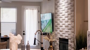 Uma sala de estar moderna com lareira, uma TV de tela plana montada em uma parede texturizada e uma área de jantar com mesa e cadeiras.