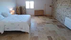 A bedroom with a bed, a dresser, a wardrobe, a radiator, and a stone wall. - Gîte Rêve de Caryan (Cuzance)