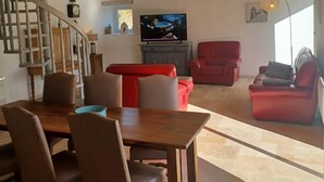A spacious living area with a wooden ceiling, a dining table with chairs, and red sofas. - Gîte Rêve de Caryan (Cuzance)