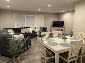Relax in this stylish living room with a dark grey sofa, dining table, and flat-screen TV.