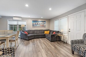 A living room with a sectional sofa, a dining table with chairs, and a patterned armchair.