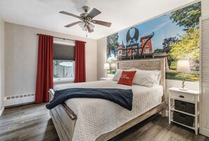 A bedroom with a bed, a ceiling fan, a nightstand, and a wall mural.