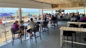 Un espace extérieur aménagé pour les repas, avec des tables et des chaises, donnant sur une plage.