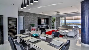 Una sala de estar moderna con comedor, televisor grande y vista al mar.