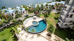 Un resort con piscina central, rodeado de palmeras y vista al mar.