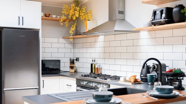 A modern kitchen with white cabinetry, a stainless steel refrigerator, a gas stove, and wooden countertops. - Prospect Cottage Ballarat (Golden Point)