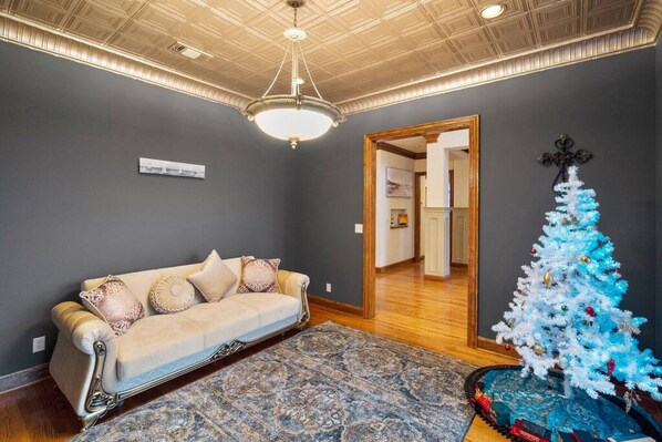 A living room with a beige sofa, a patterned rug, a blue Christmas tree, and a chandelier.
