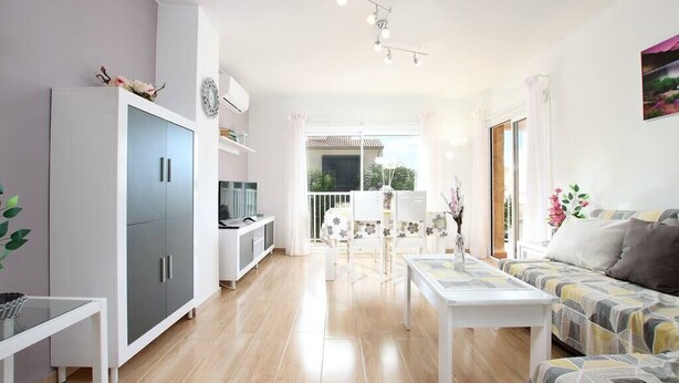 Una sala luminosa con sofá, una mesa de comedor y una zona de cocina con armarios y televisor.