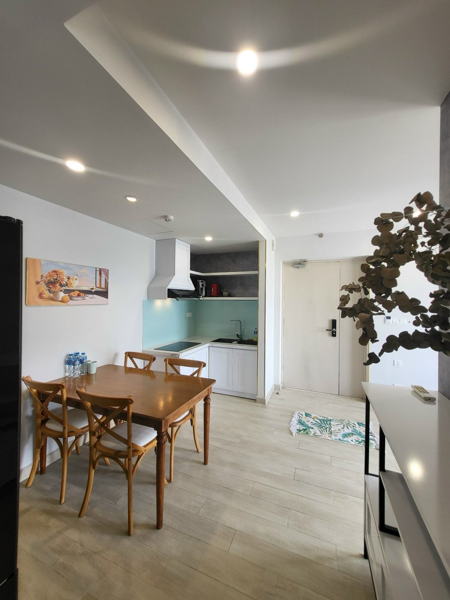 A modern kitchen with white cabinets, a built-in oven, and a microwave. There is a dining area with a wooden table and chairs.