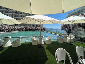 Un espace aménagé au bord de la piscine, avec des fauteuils et des parasols en osier blanc, entouré de la piscine et offrant une vue sur la mer.