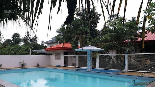 Una piscina con borde de baldosas, rodeada de una valla y palmeras.