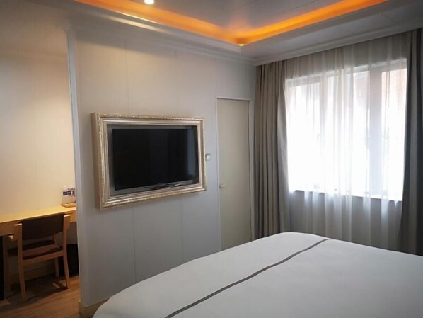 Habitación de hotel con cama, escritorio, televisor montado en la pared y ventana con cortinas.