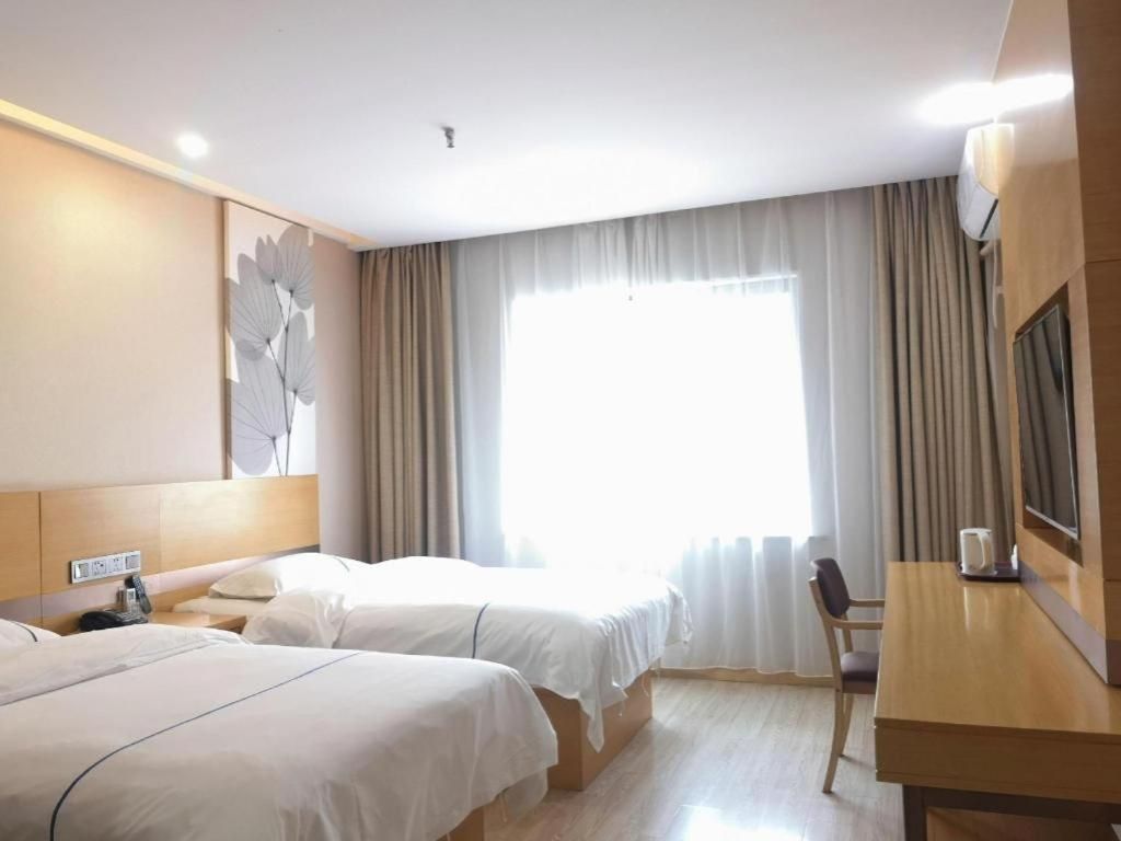 Habitación de hotel con dos camas, un escritorio, una silla y un ventanal con cortinas.
