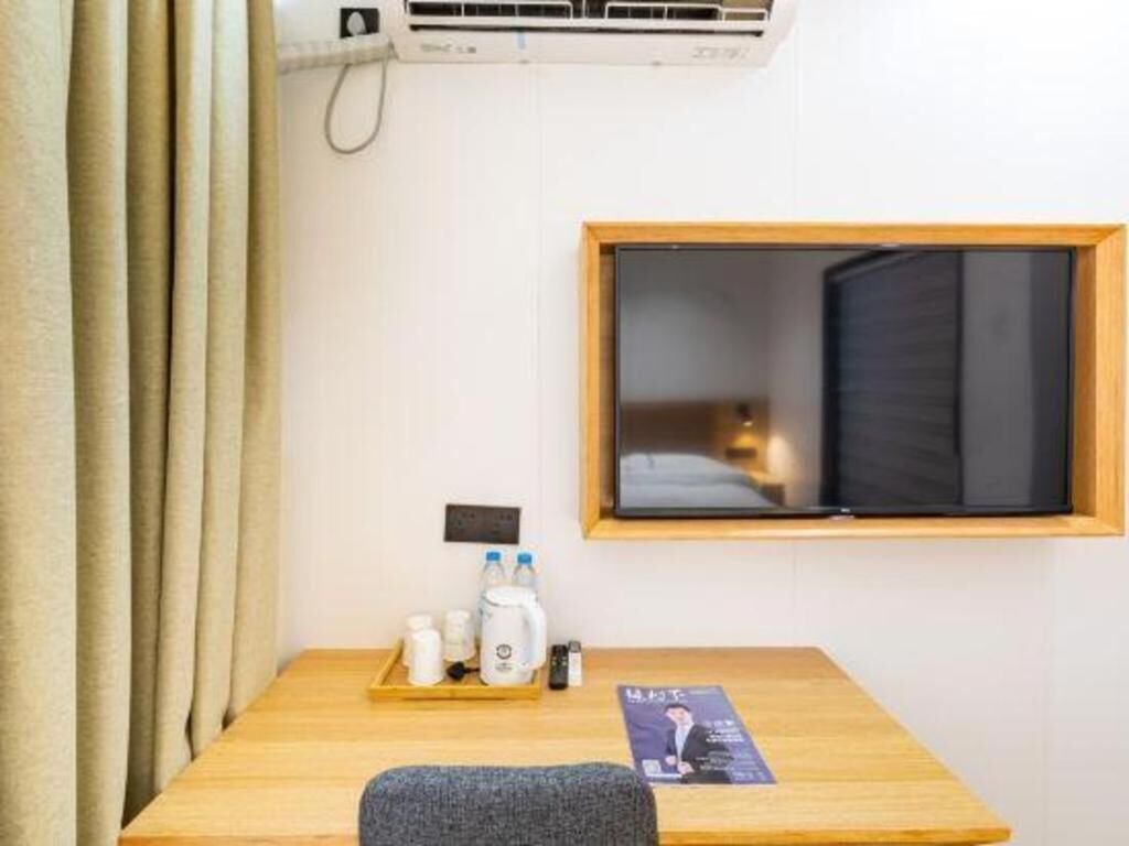 A hotel room with a wooden desk, a window with a view, and a wall-mounted air conditioner.