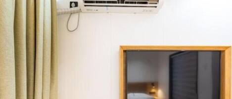 A hotel room with a wooden desk, a window with a view, and a wall-mounted air conditioner.