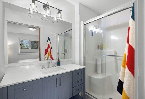 A modern bathroom with a large mirror, dual sinks, and a glass shower enclosure.
