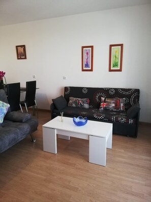 A living room with a grey sofa, a black sofa with patterned cushions, a white coffee table, and two framed pictures on the wall.